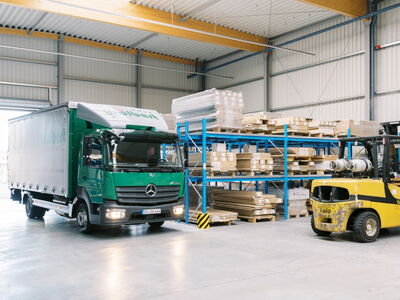Ein grüner Lkw von Sperrholz Wölbert fährt in ein Lager voller Platten und Zubehör in Dortmund. | © Wölbert